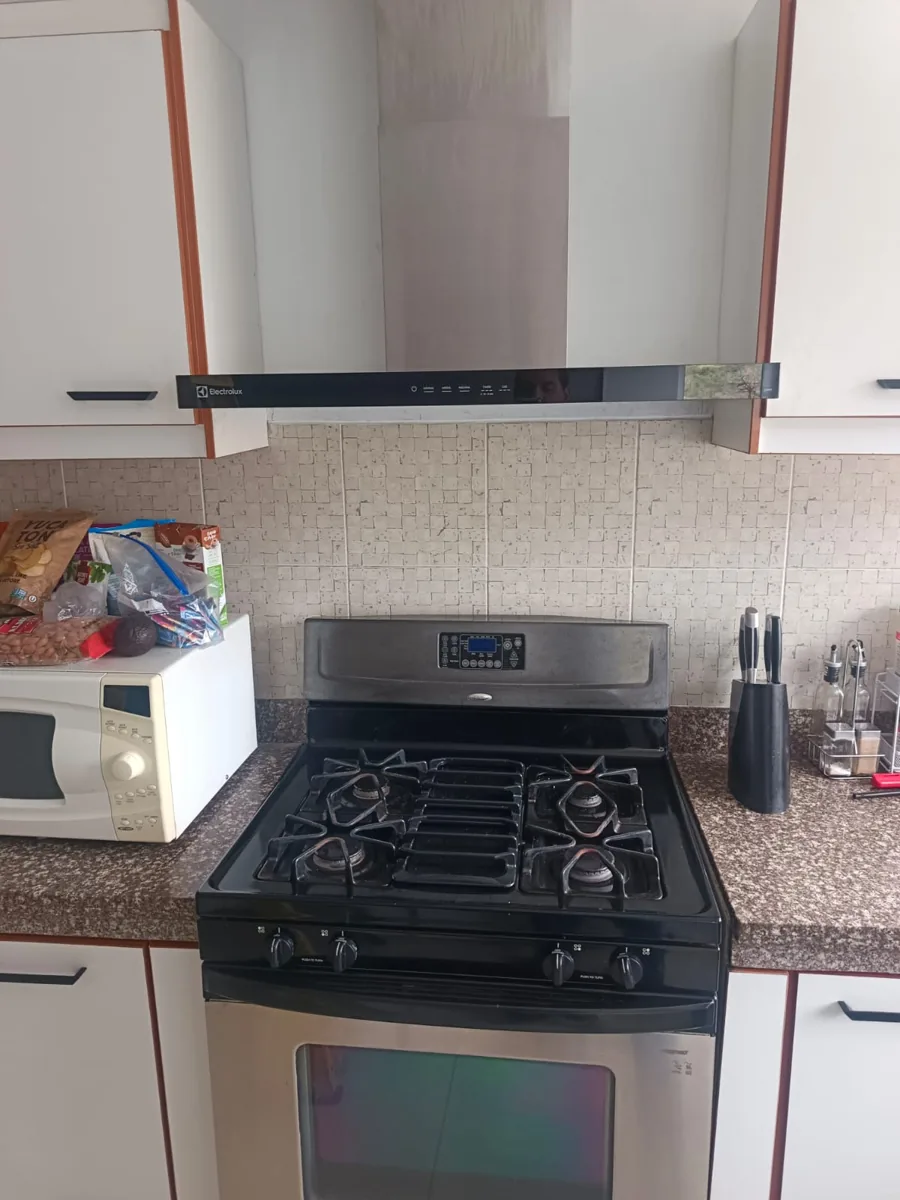 Cocina a gas negra con horno de acero inoxidable, campana extractora arriba y un microondas a la izquierda