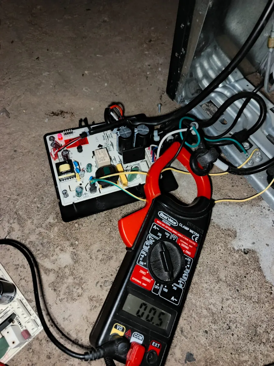 Pinza amperimétrica junto a una tarjeta electrónica desmontada sobre el piso
